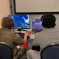 Two GVSU students have headphones on and are watching something on a computer screen.